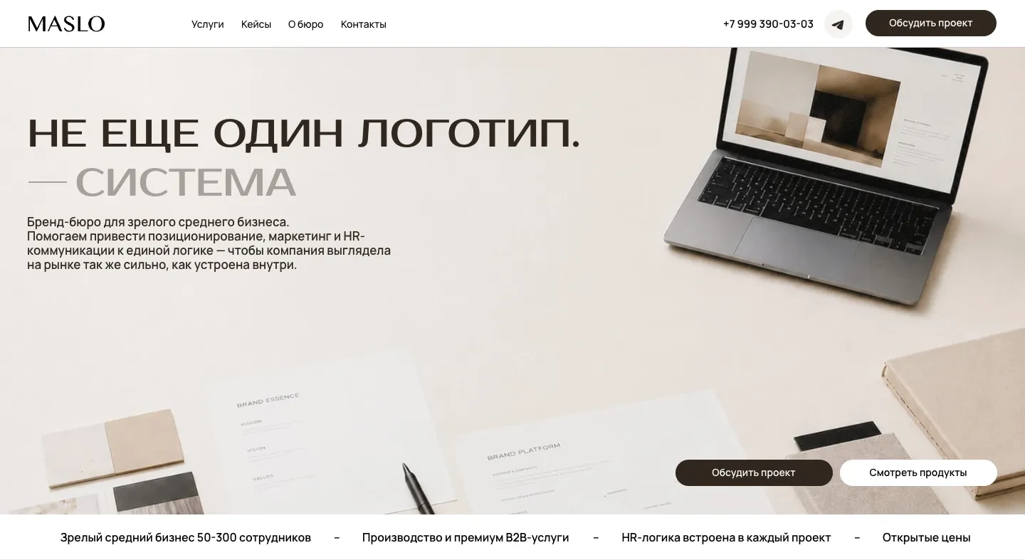Первый экран сайта MASLO: заголовок «Не еще один логотип. Система», подзаголовок о бренд-бюро, фото ноутбука и бумаг бренд-платформы на столе, кнопки «Обсудить проект» и «Смотреть продукты»